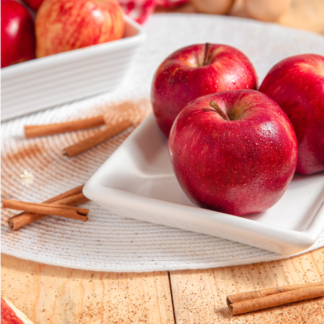 red apples in a white dish on wooden table with cinnamon sticks