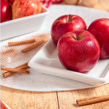 red apples in a white dish on wooden table with cinnamon sticks